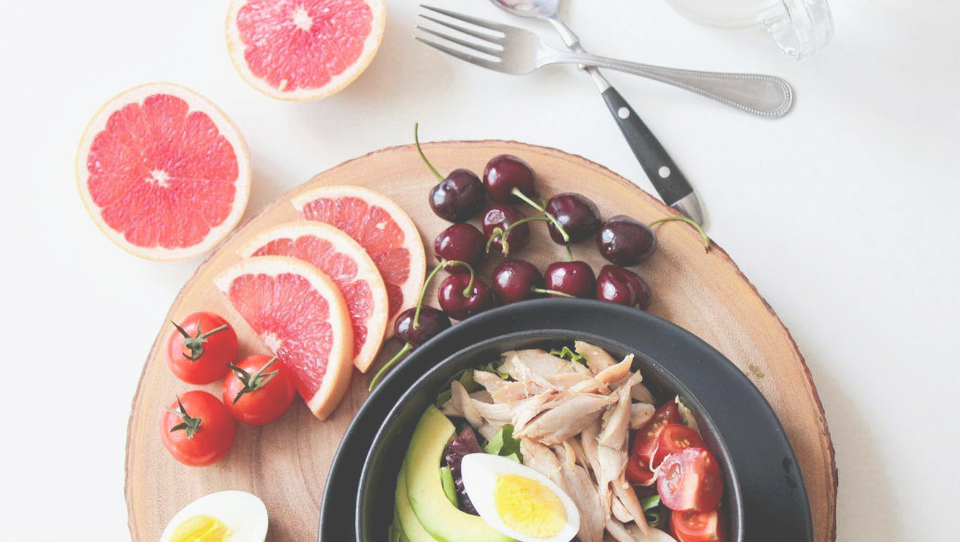 Colorful meal with grapefruit, cherries, tomatoes, avocado, and chicken